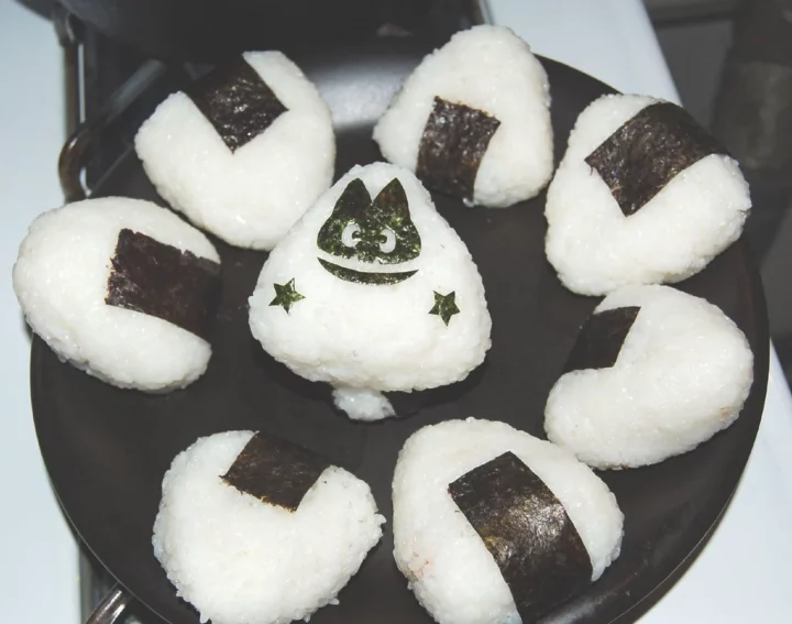 a plate of onigiris with the middle one having a face drawn on it using nori