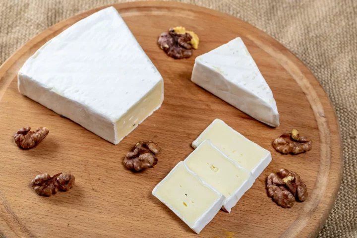 pieces of brie in different shapes placed on a wooden tray with walnuts